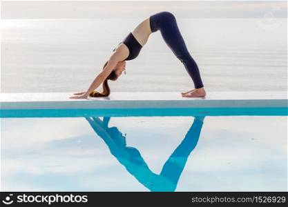 woman practice yoga Downward Facing dog or yoga Adho Mukha Svanasana pose meditation summer vacation on the pool,Travel in tropical beach Thailand,vacations and relaxation Concept