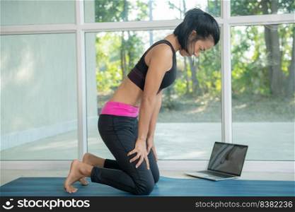 woman practicing yoga, doing upward abdominal lock exercise, uddiyana Bandha pose,  working out, wearing sportswear, watching fitness video tutorial online on laptop, doing workout at home sitting.