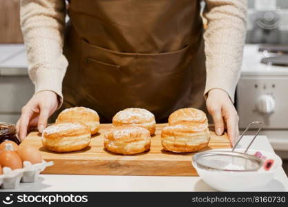 Woman prepares fresh donuts with jam in home kitchen. Cooking traditional Jewish Hanukkah sufganiyot. Hands sprinkle Berliners with powdered sugar.. Woman prepares fresh donuts with jam in home kitchen. Cooking traditional Jewish Hanukkah sufganiyot. 