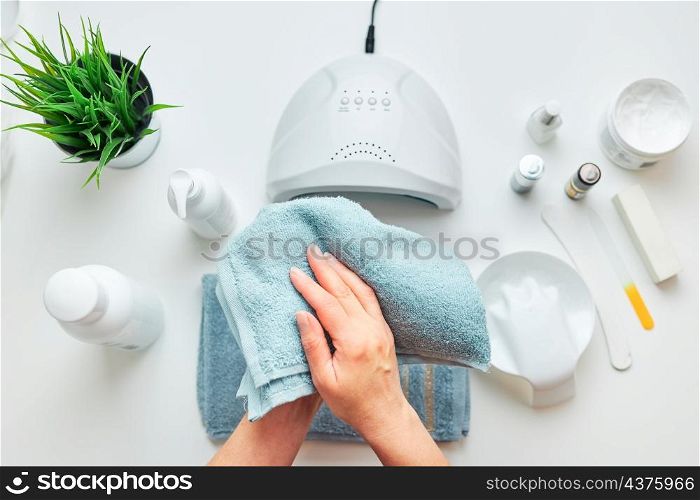 Woman preparing nails to apply gel hybrid polish using UV lamp. Beauty wellness spa treatment concept. Cosmetic products, UV lamp, green leaves on white table. Spa, manicure, skin care concept. Flat lay, overhead view