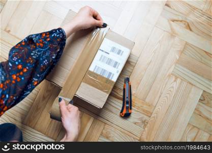 Woman preparing online order. Packing parcel to send using cardbox, tape and knife