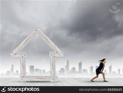 Woman pulling house. Young determined businesswoman pulling wooden house model