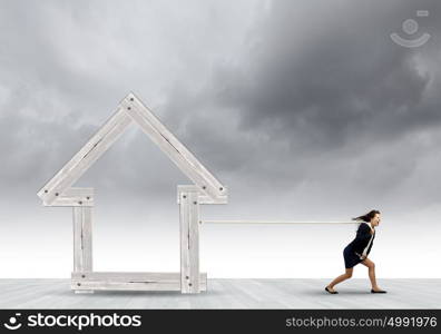 Woman pulling house. Young determined businesswoman pulling wooden house model