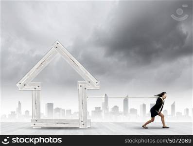 Woman pulling house. Young determined businesswoman pulling wooden house model