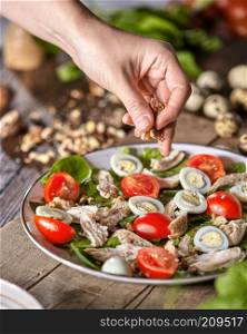 Woman put nuts to a freshly prepared homemade salad from organic ingredients on a wooden board. Natural freshly organic dieting food.. Female hand puts walnuts to the plate of freshly cooked salad from natural ingredients on a wooden table. Healthy diet eat.
