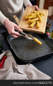 Woman puts cheese sticks into hot oiled grill frying pan.. Woman puts cheese sticks into hot oiled grill frying pan