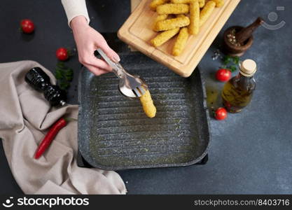 Woman puts cheese sticks into hot oiled grill frying pan.. Woman puts cheese sticks into hot oiled grill frying pan