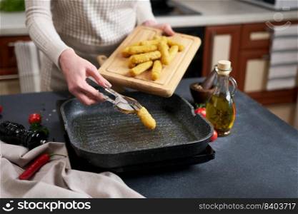 Woman puts cheese sticks into hot oiled grill frying pan.. Woman puts cheese sticks into hot oiled grill frying pan