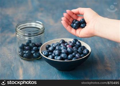 Woman putting freshly gathered blueberries from a jar into a small bowl. Table painted in blue in the background