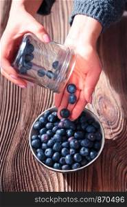 Woman putting freshly gathered blueberries from a jar into a small bowl. Dish put on old wooden table. Shot from above