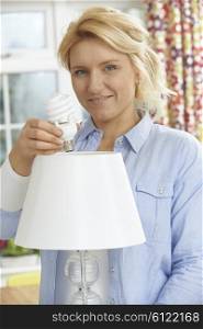 Woman Putting Low Energy Lightbulb Into Lamp At Home