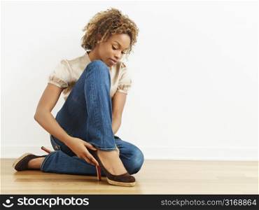 Woman putting on high heel shoes sitting on wood floor.
