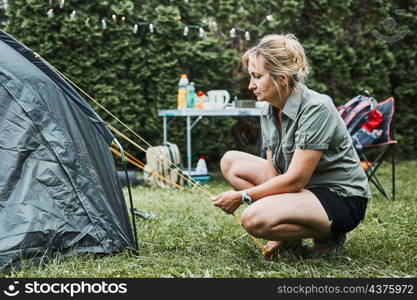 Woman putting up a tent at camping during summer vacation. Female preparing campsite to rest and relax. Spending vacations outdoors close to nature