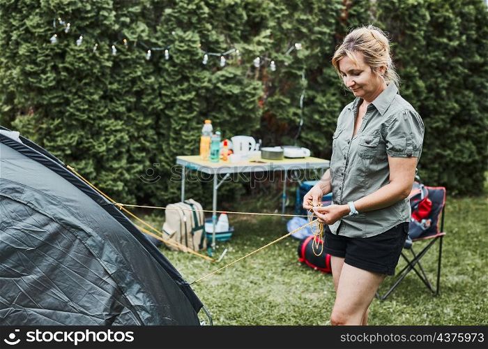 Woman putting up a tent at camping during summer vacation. Female preparing campsite to rest and relax. Spending vacations outdoors close to nature