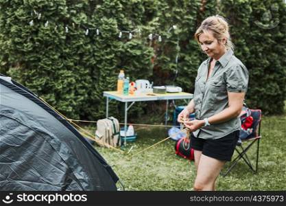 Woman putting up a tent at camping during summer vacation. Female preparing campsite to rest and relax. Spending vacations outdoors close to nature