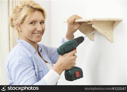 Woman Putting Up Wooden Shelf At Home Using Cordless Drill