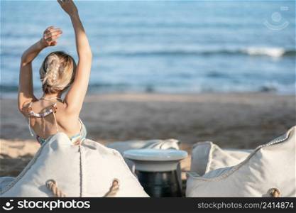 Woman raised hands up in the sky, relaxing on bean bag beach chair near the beach.