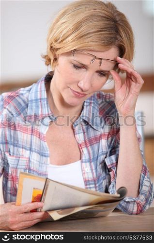 Woman raising her glasses to read something in a magazine