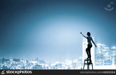 Woman reaching hand up. Businesswoman standing on chair and reaching hand to touch something