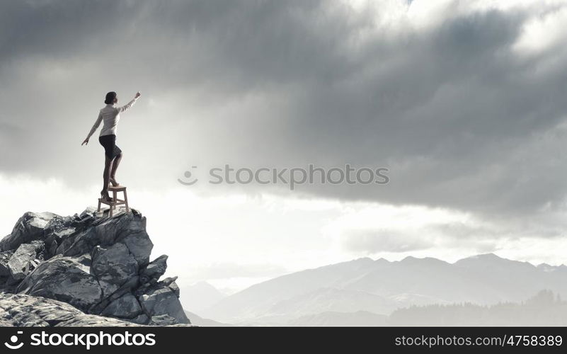 Woman reaching hand up. Businesswoman standing on chair and reaching hand to touch something