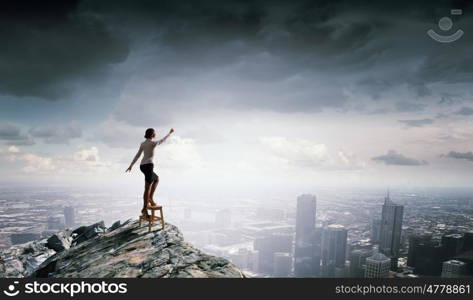 Woman reaching hand up. Businesswoman standing on chair and reaching hand to touch something