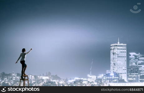 Woman reaching hand up. Businesswoman standing on chair and reaching hand to touch something