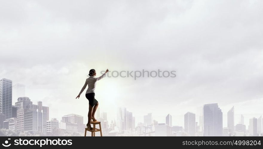 Woman reaching hand up. Businesswoman standing on chair and reaching hand to touch something