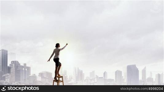 Woman reaching hand up. Businesswoman standing on chair and reaching hand to touch something