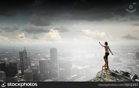 Woman reaching hand up. Businesswoman standing on chair and reaching hand to touch something