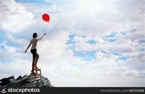 Woman reaching hand up. Businesswoman standing on chair and reaching hand with balloon