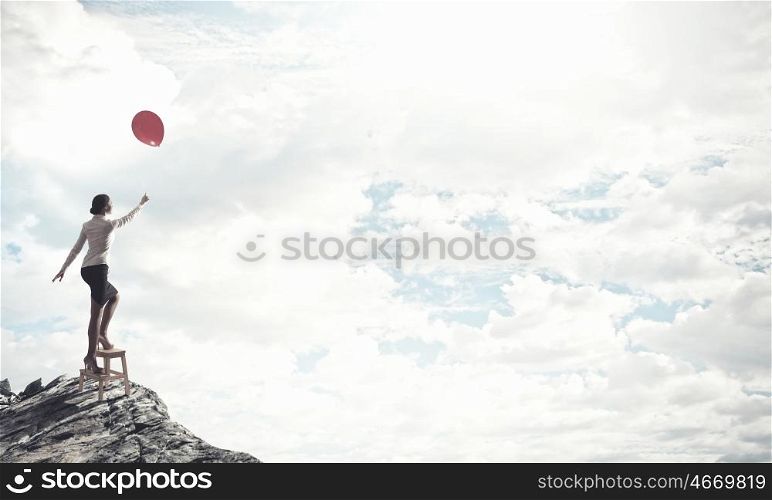 Woman reaching hand up. Businesswoman standing on chair and reaching hand with balloon