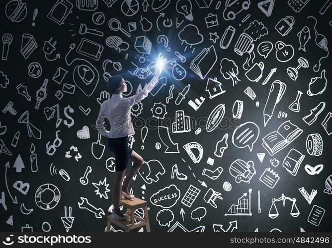 Woman reaching hand up . Businesswoman standing on chair and reaching light spot