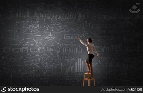 Woman reaching hand up. Woman standing on chair and reaching hand to chalkboard