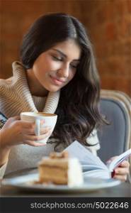 Woman reading a book at cafe while having hot latte coffee and tasty cake