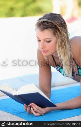 Woman reading a book by the poolside