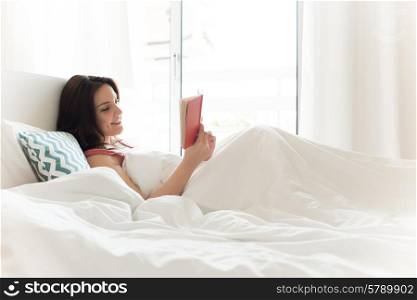 Woman reading book in bed during the morning