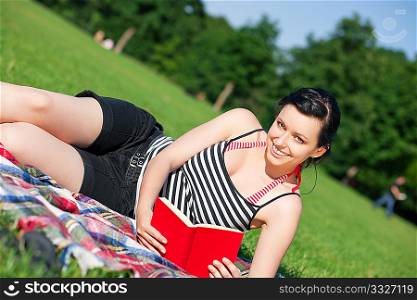 Woman reading book in the sunshine lying on a meadow in summer