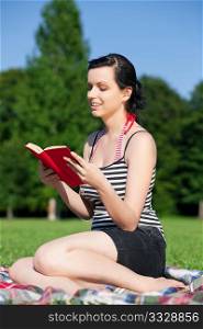 Woman reading book in the sunshine sitting on a meadow in summer