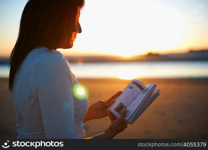Woman reading book on Cannon Beach at sunset, California, USA