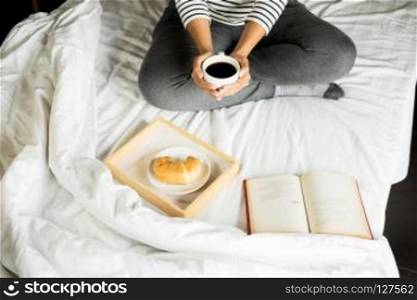 Woman reading book or newspaper and drinking coffee breakfast on bed during the morning.. Woman reading book or newspaper and drinking coffee breakfast on