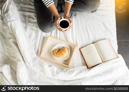 Woman reading book or newspaper and drinking coffee breakfast on bed during the morning.. Woman reading book or newspaper and drinking coffee breakfast on