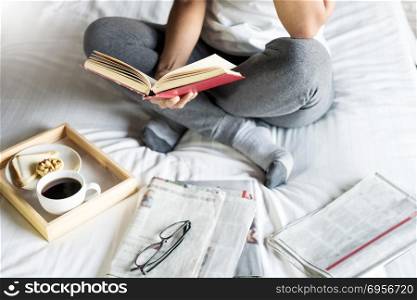 Woman reading book or newspaper and drinking coffee breakfast on bed during the morning. Woman reading book or newspaper and drinking coffee breakfast on