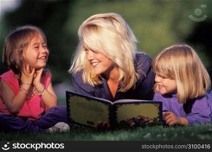 Woman reading book to girls in grass