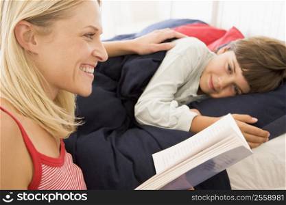 Woman reading book to young boy in bed smiling