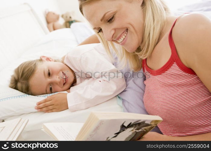 Woman reading book to young girl in bed smiling