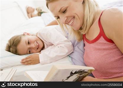 Woman reading book to young girl in bed smiling