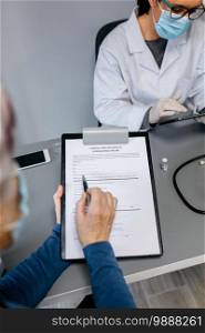 Woman reading consent form for coronavirus vaccine with her doctor