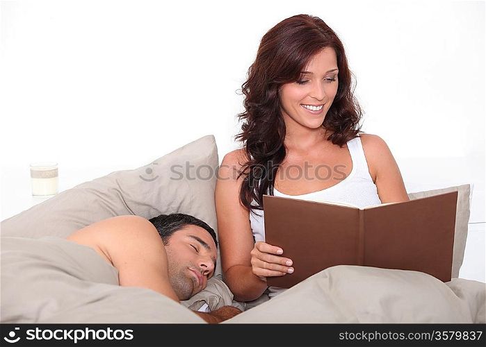 Woman reading in bed as her partner sleeps