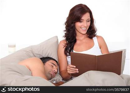 Woman reading in bed as her partner sleeps