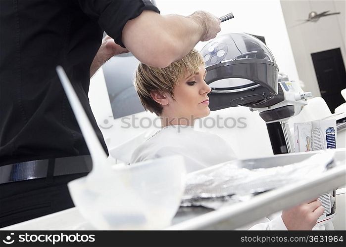 Woman reading magazine while hairdresser coloring hair